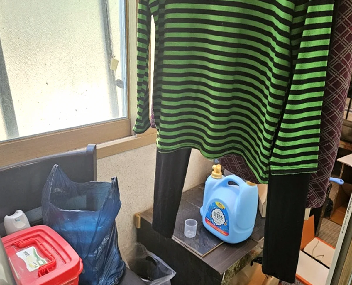 정리 전 베란다 — 창가에 걸린 줄무늬 옷과 의자 위 반찬통·섬유유연제 통