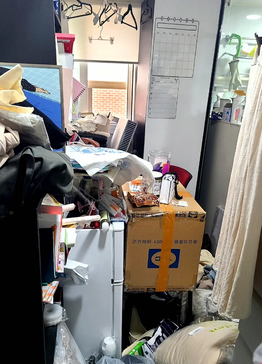정리 전 원룸텔 입구 — 바닥에 비닐봉지와 베개, 옷 더미가 쌓여 발 디딜 틈 없는 모습