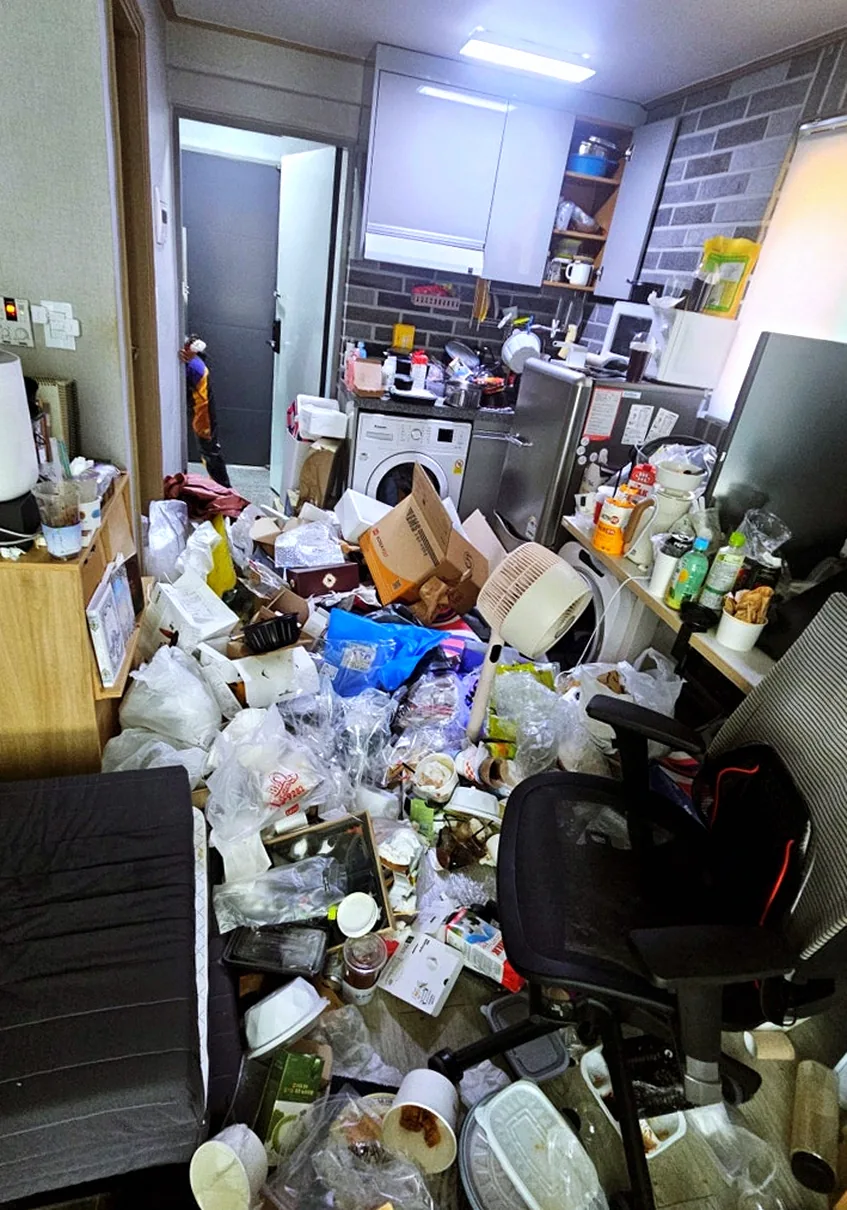 창 쪽에서 본 현관 방향 — 바닥에 뒤엉킨 컵과 배달 그릇, 플라스틱 용기