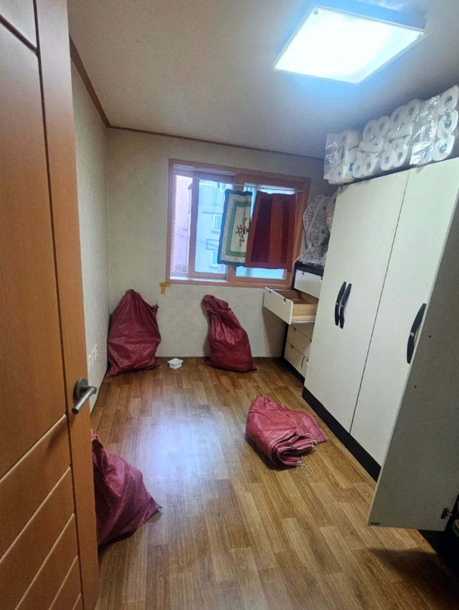 정리 전 첫 번째 방 — 흰 옷장 위에 두루마리 휴지 묶음이 천장까지 쌓이고 바닥에 빨간 마대자루