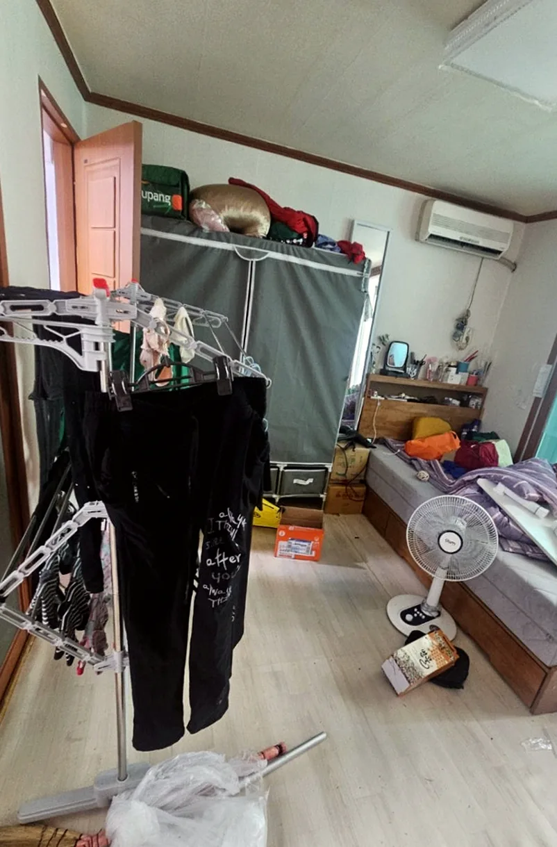 정리 전 침실 — 빨래건조대에 걸린 옷과 침대 위 뒤엉킨 이불