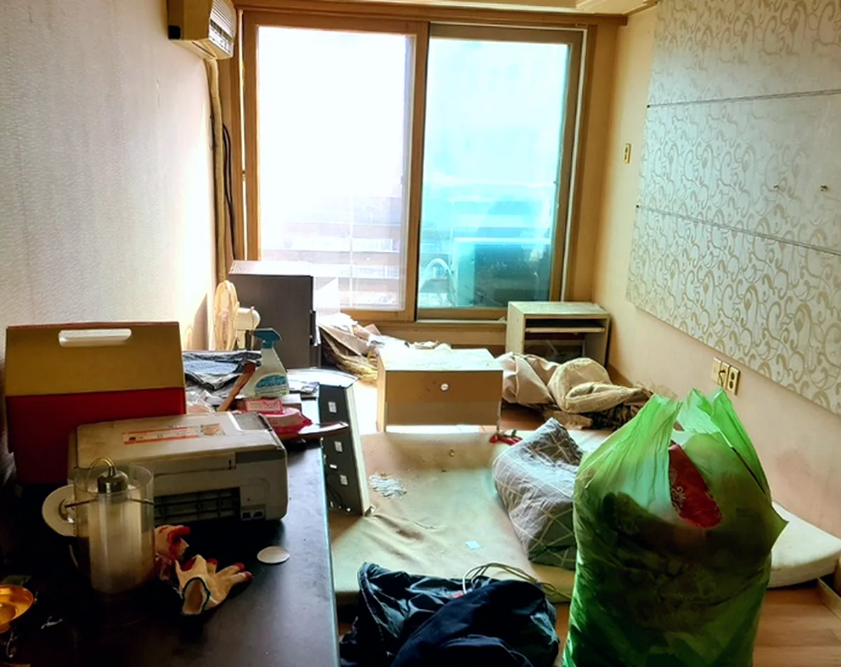 정리 전 거실 — 통창 앞 매트 위에 연두색 대형 봉투와 이불, 장식장 위 아이스박스와 프린터