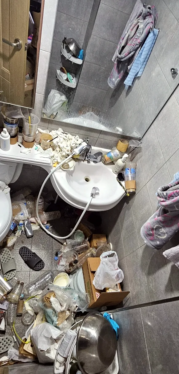 정리 전 화장실 — 세면대 위 휴지 뭉치와 바닥의 페트병·비닐·상자