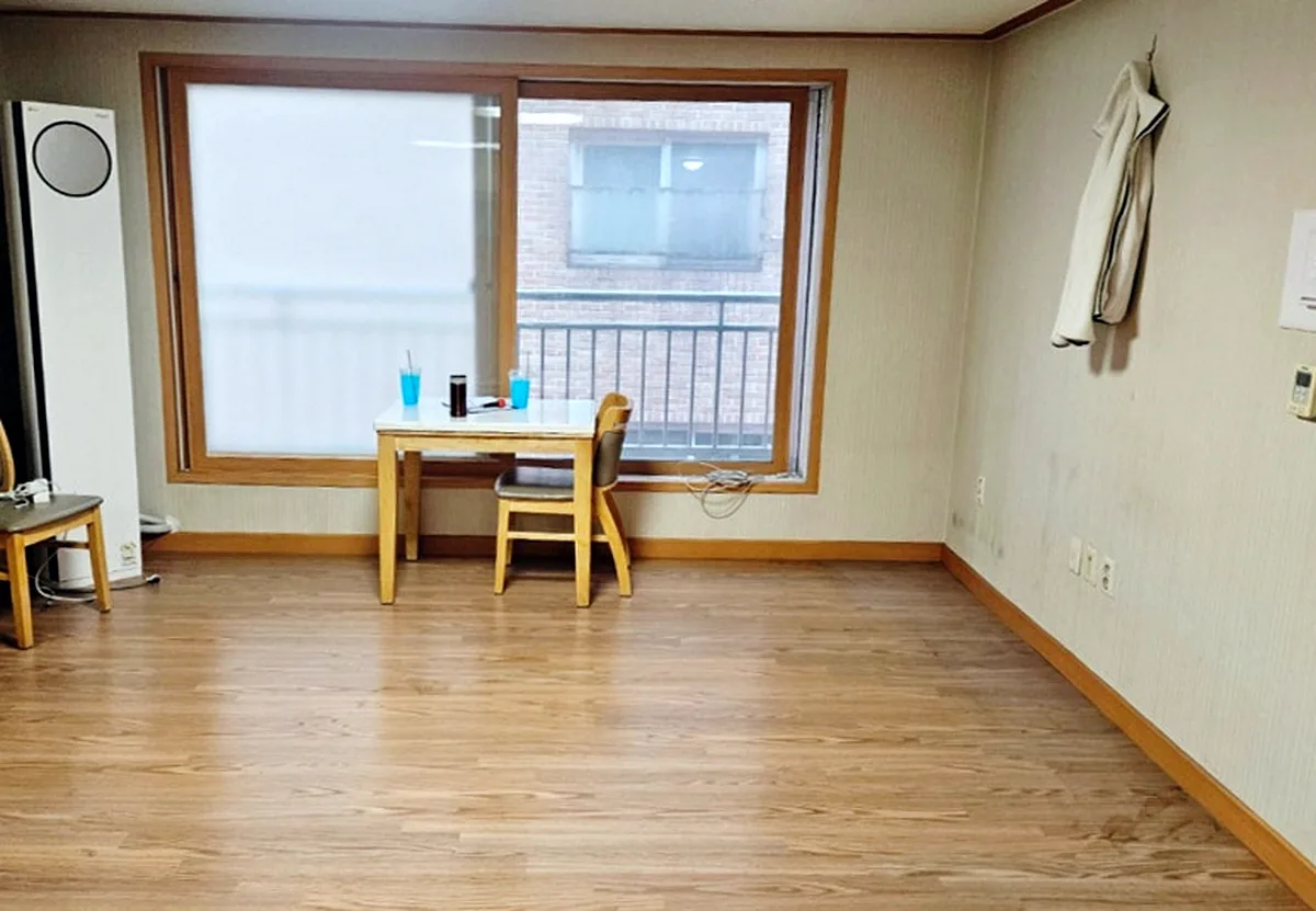 정리 후 거실 — 소파와 흔들의자를 빼고 2인 식탁과 의자, 스탠드 에어컨만 남긴 모습